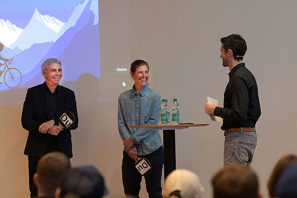 Zwei Männer und eine Frau stehen auf einer Bühne.