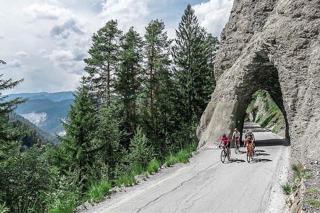 Eine Gruppe Radfahrer fährt unter einem Fels durch einen Tunnel.