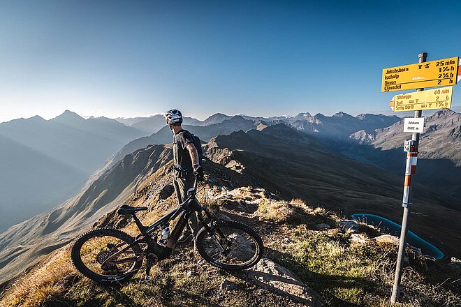 Ein Mann steht auf einem Berggipfel und Blickt ins Tal.