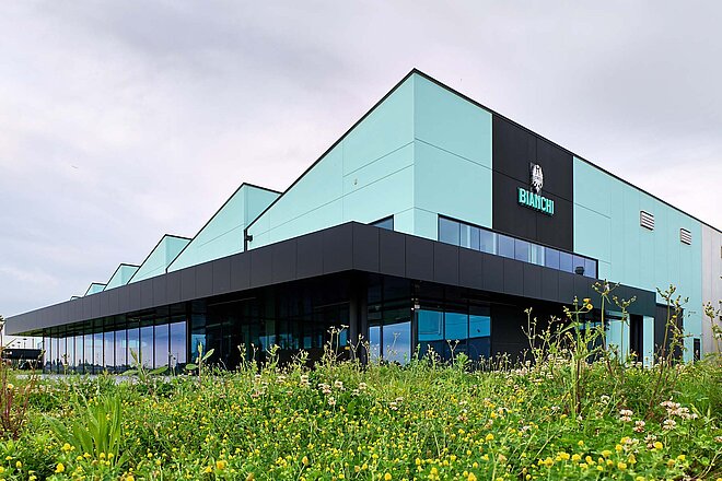 Binachi Fahrradfabrik Italien. Fabrikhalle mit grünen Wänden, davor eine Blumenwiese.