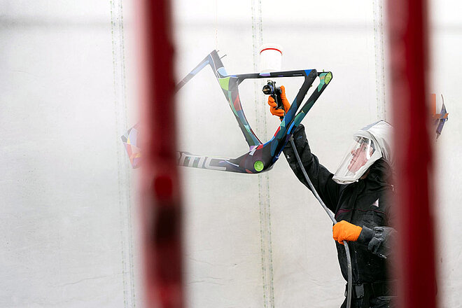 Ein Lackierer trägt Farbe auf einen Fahrradrahmen von BMC auf.