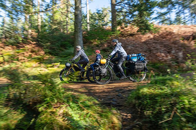 Tern Orox Adventure Cargobike. Eine Familie fährt mit Fahrrädern durch den Wald.