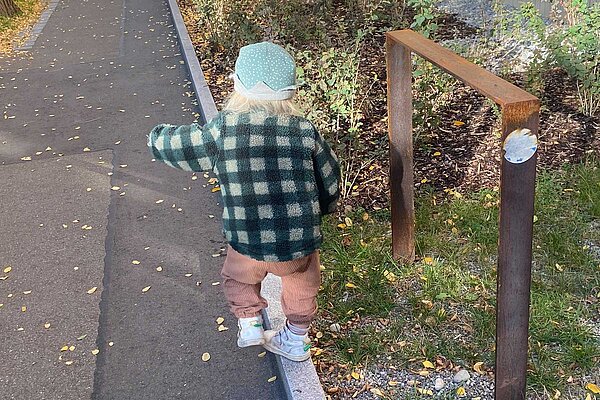 Kleinkind im Karofleece balanciert auf Mäuerchen.