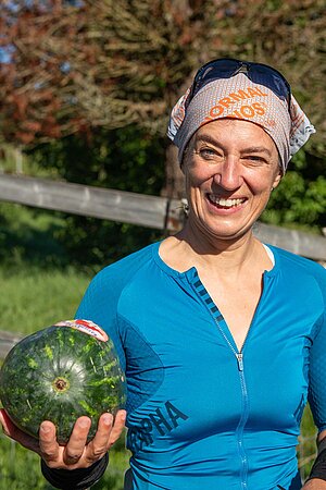 Eine Frau mit blauem Radtricot hält eine Melone in der Hand. 