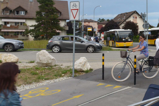 Veloweg mit Velofahrerin und Postautos im Hintergrund