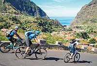 Drei Personen fahren mit Mountainbikes auf einer Strasse.