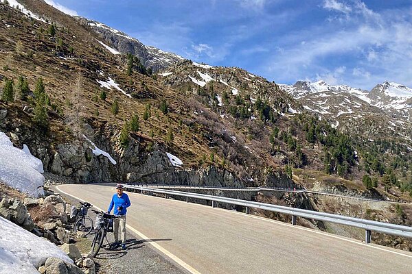 Ein Radfahrer steht am Strassenrand einer Passstrasse in den Alpen.