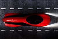 Ein rotes vollverschaltes Velomobil auf einem Fahrradweg.