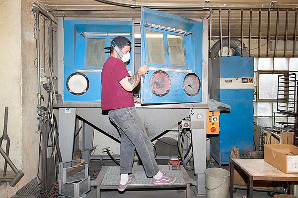 Ein Mann mit rotem T-Shirt steht an einer Maschine in einer Werkstatt.