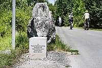 Entlang der Vorarlberger Radroute Nr. 1 erinnern 52 Hörstationen an Fluchtgeschichten von 1938 bis 1945. Stein mit Tafel neben einem Radweg.