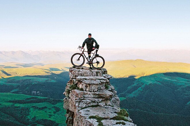 Mann steht mit Fahrrad auf Bergspitze. 