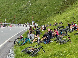 Radfahrer sitzen auf einer Wiese am Strassenrand. 
