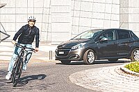 Ein Mann fährt mit dem Fahrrad durch einen Kreisverkehr, ihm folgt ein Auto.