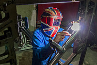 Orange Bikes ist insolvent. Eine Person mit Schweissmaske schweisst einen Fahrradrahmen.