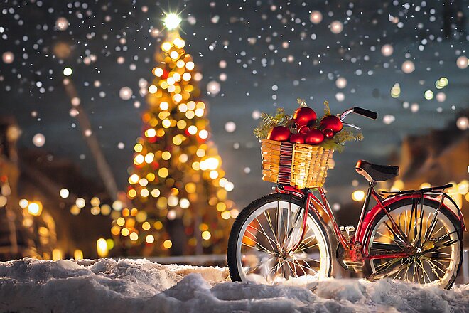 Rotes Velo mit Geschenkkorb am Lenker im Schnee vor Christbaum und Nachthimmel