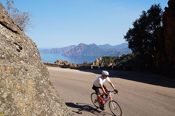 Mit dem Rennrad durch Korsika. Radfahrer auf Bergstrasse, im Hintergrund das Meer.