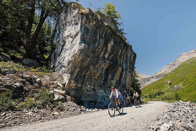 Gravelbiker überqueren eine Kiesstrasse in den Alpen.