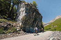 Gravelbiker überqueren eine Kiesstrasse in den Alpen.