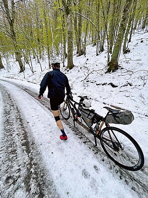 Tandem Fahrrad Reise Italien. Eine Person schiebt ein Fahrrad durch den Schnee.