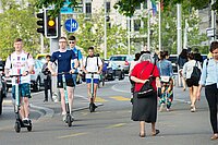 Eine Fussgängerzone mit Tretroller Fahrern und Fussgängern