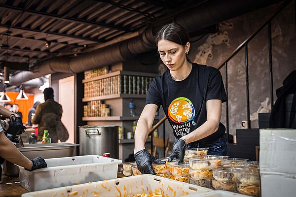 Tern spendet 1 Prozent des Gewinns. Eine Frau mit T-Shirt und Latexhandschuhen verteilt Essen. 