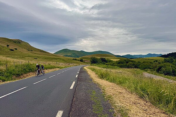 Radfahrer auf einsamer Landstrasse. Im Hintergrund grüne Hügel.
