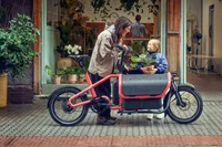 Eine Frau steht mit einen Kinden neben einem Lastenrad von Riese & Müller.