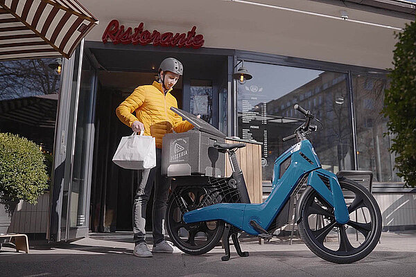 Ein Mann mit gelber Jacke steht hinter einem blauen E-Bike