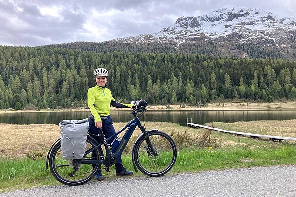 Eine Frau mit gelbem Fahrradtricot steht neben ihrem E-Bike.