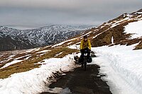 Tipps Velofahren im Winter. Ein Mann mit gelber Jacke fährt mit dem Fahrrad auf einer verschneiten Strasse. 