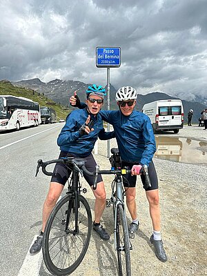 Zwei Radfahrer posieren vor dem Schild auf einer Passhöhe.
