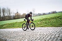 Rennradfahrer mit schwarzer Kleidung fährt über Kopfsteinpflaster