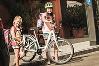 Zwei Mädchen queren auf dem Weg zur Schule die Strasse mit weissem Fahrrad