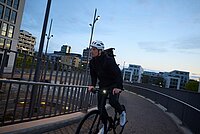 Mann mit weissem Uvex Velohelm fährt in der Dämmerung einer Brück entlang