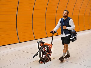Brompton G Line. Ein Mann schiebt ein Faltvelo von Brompton auf einem Bahnsteig.
