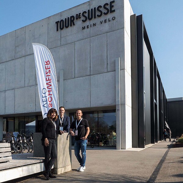 Eine Frau und zwei Männer posieren vor einem Gebäude für ein Foto