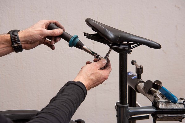 Eine Person schraubt mit einem Drehmomentschlüssel Schrauben am Fahrradsattel fest