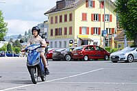 Ein Mann mit T-Shirt und kurzen Hosen fährt auf einem E-Roller.