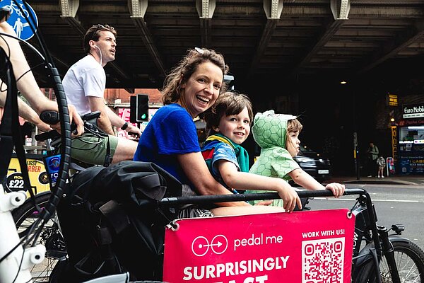 London 60 Prozent mehr Cargobikes. Eine Frau und zwei Kinder sitzen in der Transportkiste eines Lastenrads.
