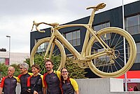 Ein goldenes Rennrad steht auf einem Betonsockel. 