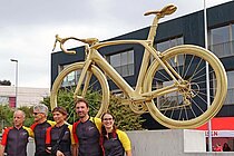 Ein goldenes Rennrad steht auf einem Betonsockel. 