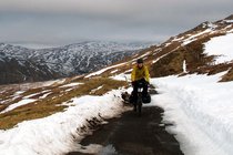 Tipps Velofahren im Winter. Ein Mann mit gelber Jacke fährt mit dem Fahrrad auf einer verschneiten Strasse. 