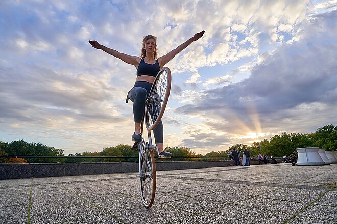 Eine Kunstrad-Fahrerin balanciert mit ihrem Velo auf dem Hinterrad. 