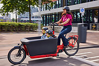Trek Fetch Cargobikes. Eine Frau transportiert zwei Kinder in einem roten Lastenrad. 