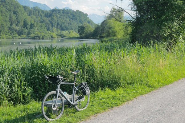 Locker durch die Schweiz radeln: Vier Routen zwischen Bodensee und Genfersee. Ein Rennrad steht am Ufer eines Sees auf einer grünen Wiese.