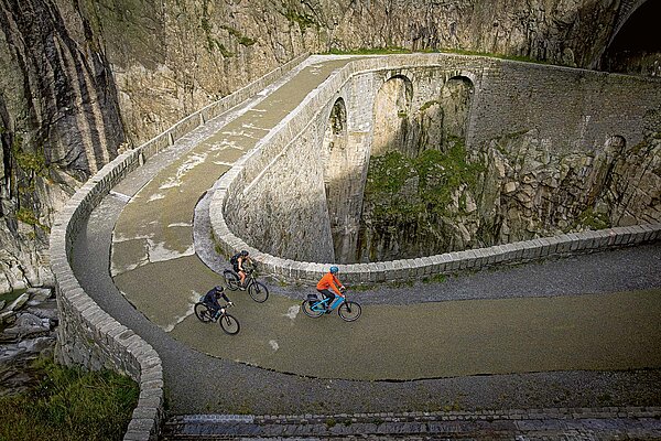 Drei Personen fahren mit Velos über eine Steinbrücke.
