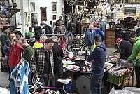 Der Teilchenbeschleuniger ist der grösste Secondhand und Veloteile Flohmarkt der Schweiz. Viele Menschen stehen in einem Raum, auf Tischen liegen Kleider und Fahrradteile zum Verkauf.