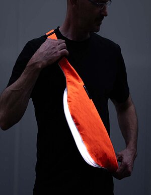 Eine Person mit schwarzem T-Shirt trägt eine orange leuchtende Tasche. 