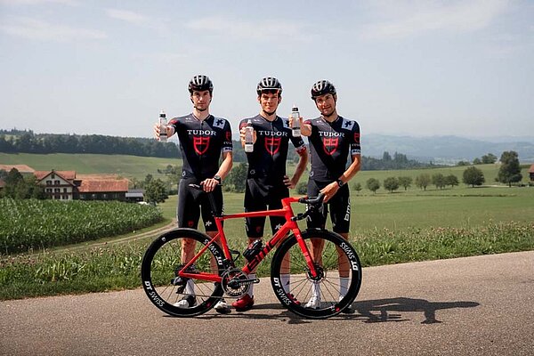 KA-EX Tudor Pro Cycling Partnerschaft. Rennradfahrer halten Wasserflaschen in die Höhe.