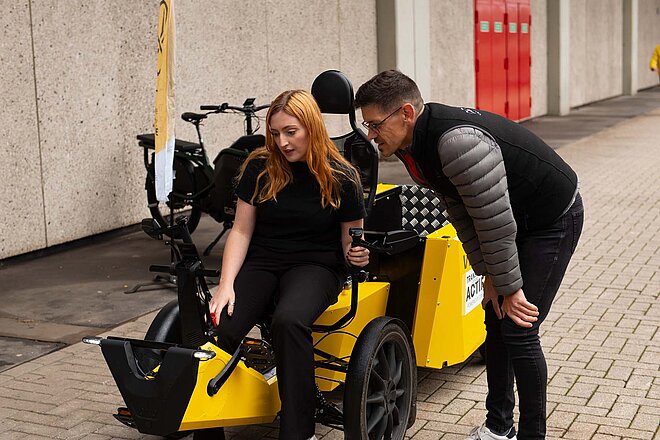 Eine Frau mit roten Haaren sitzt auf einem Lastenrad. 